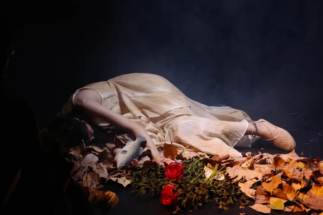 A performer lies among leaves and red roses during AWAKE.