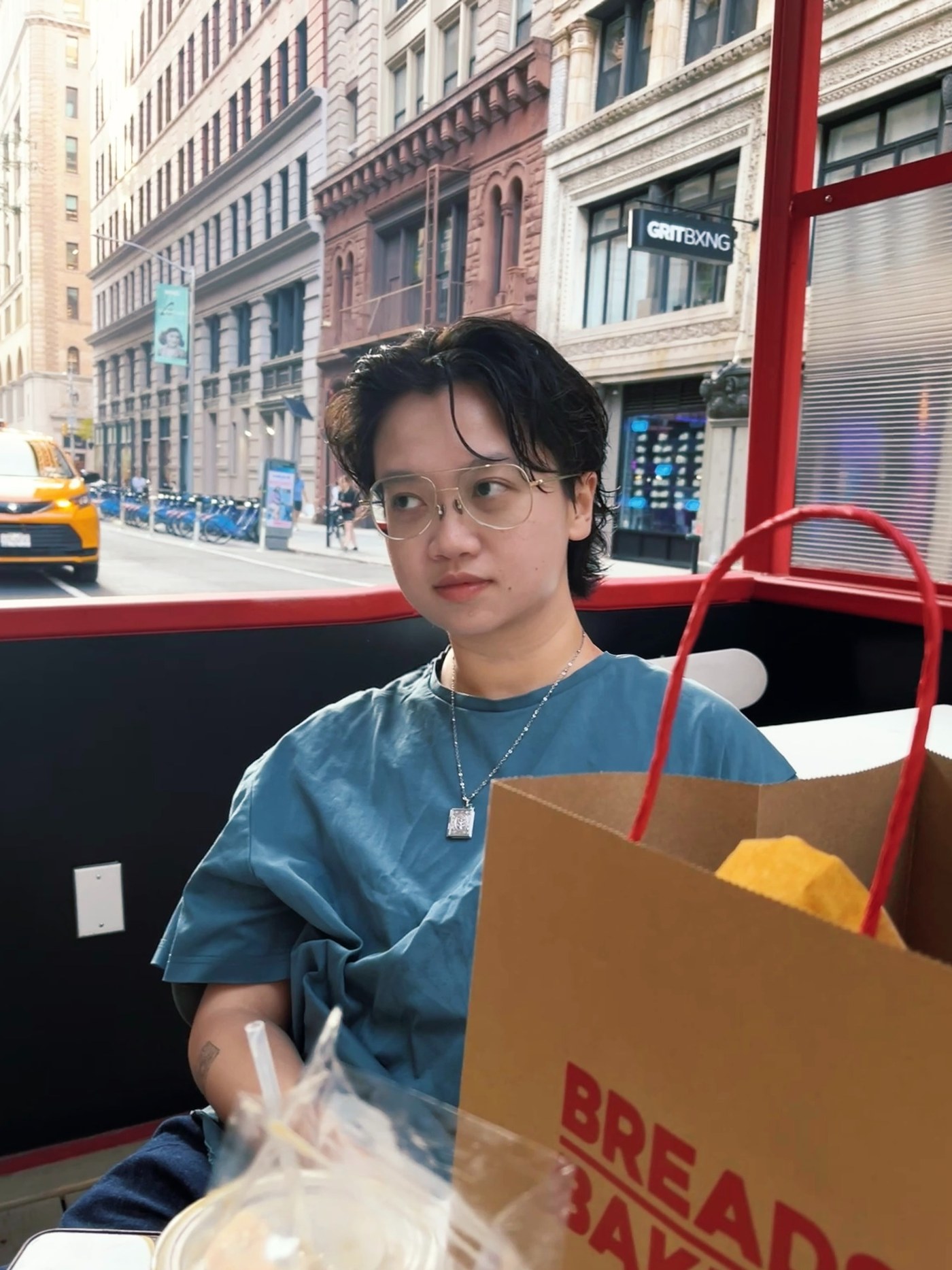 Melvin seated on a red open-top bus in New York City, looking off to the side.